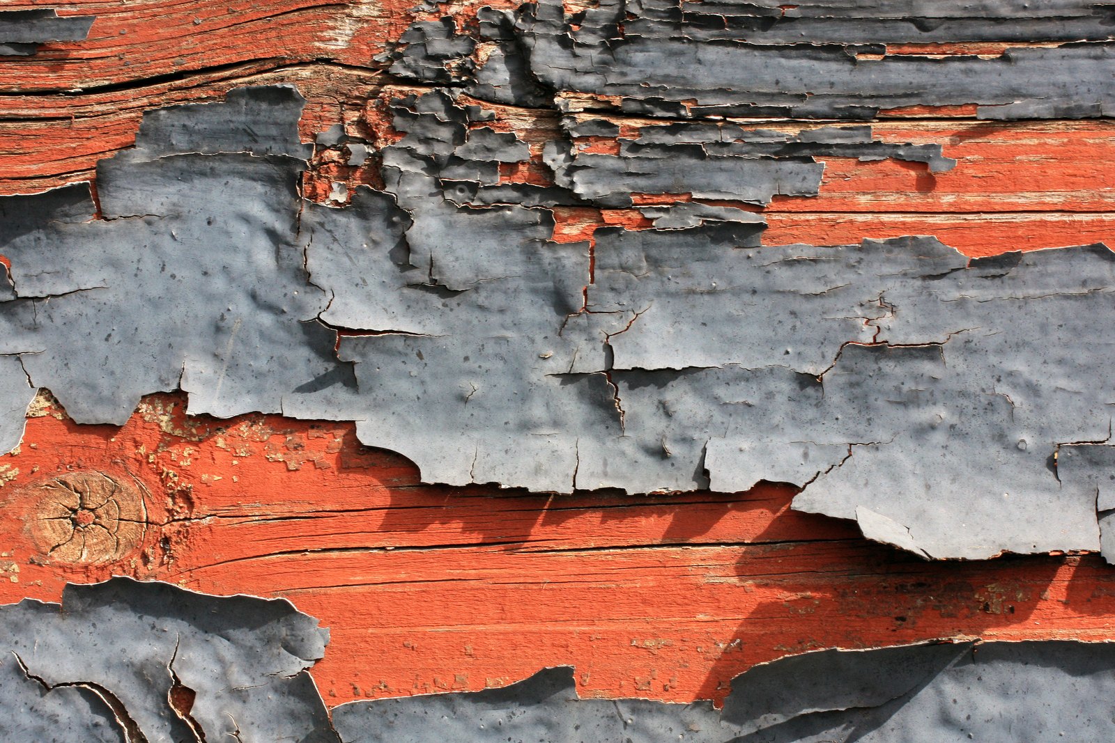 Gray paint lifting in large flakes from a red painted wooden surface.