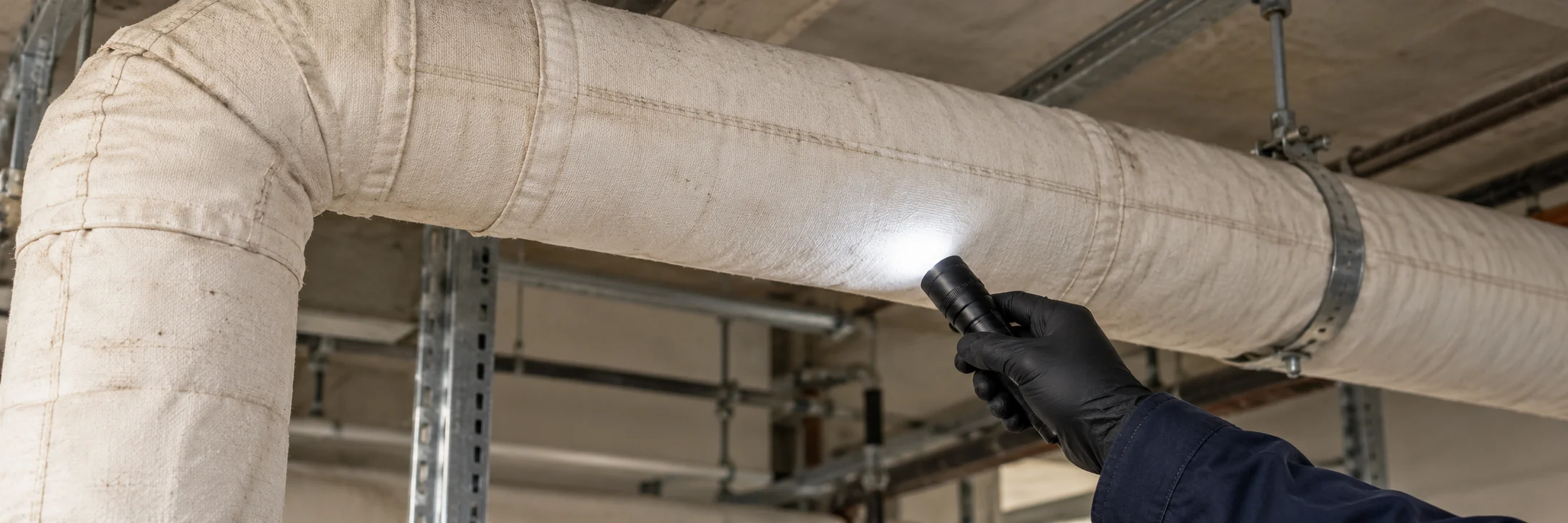 Mano con guante iluminando aislamiento intacto de tuberías durante una inspección de materiales de construcción
